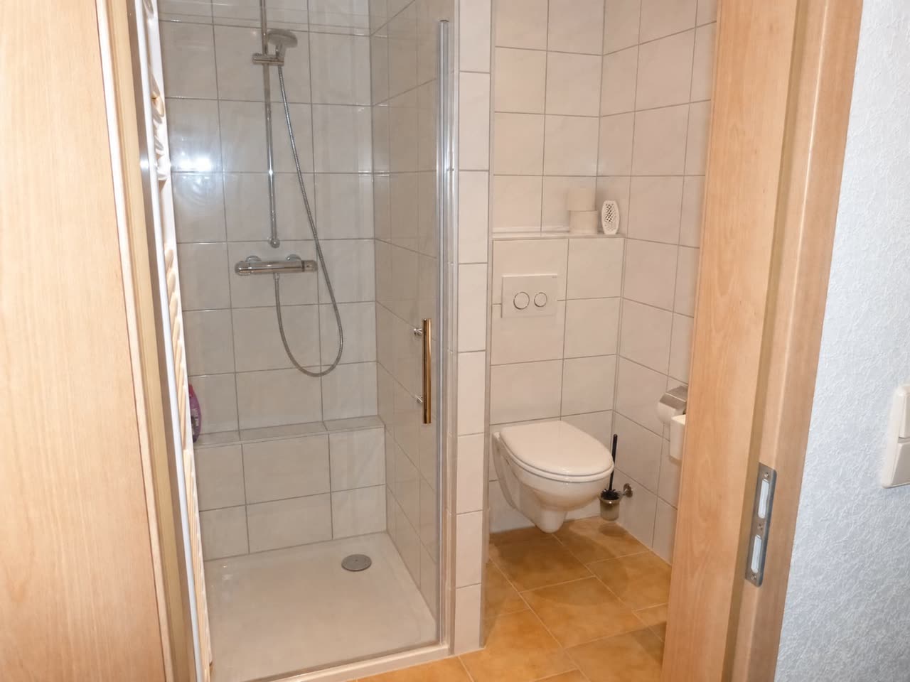 Badezimmer der Pension mit verglaster Duschkabine und wandhängendem WC