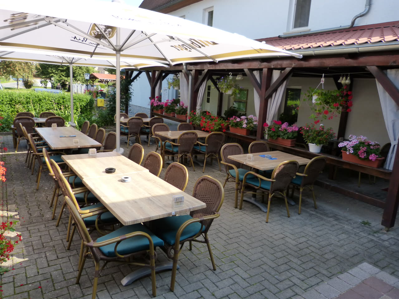 Der überdachte Terrassenbereich an der Hausfassade mit Holzpergola und Tischen darunter
